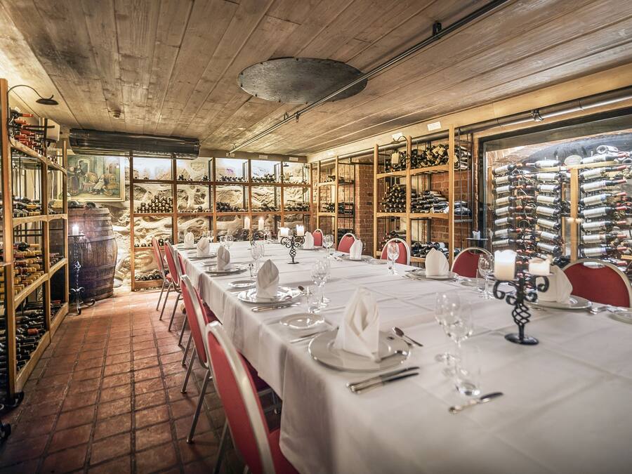 A long dining table set with white tablecloths, wine racks, and a brick wall.