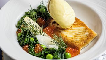 A white plate with a piece of fish, greens, and roe, and a spoon with a scoop of sauce.