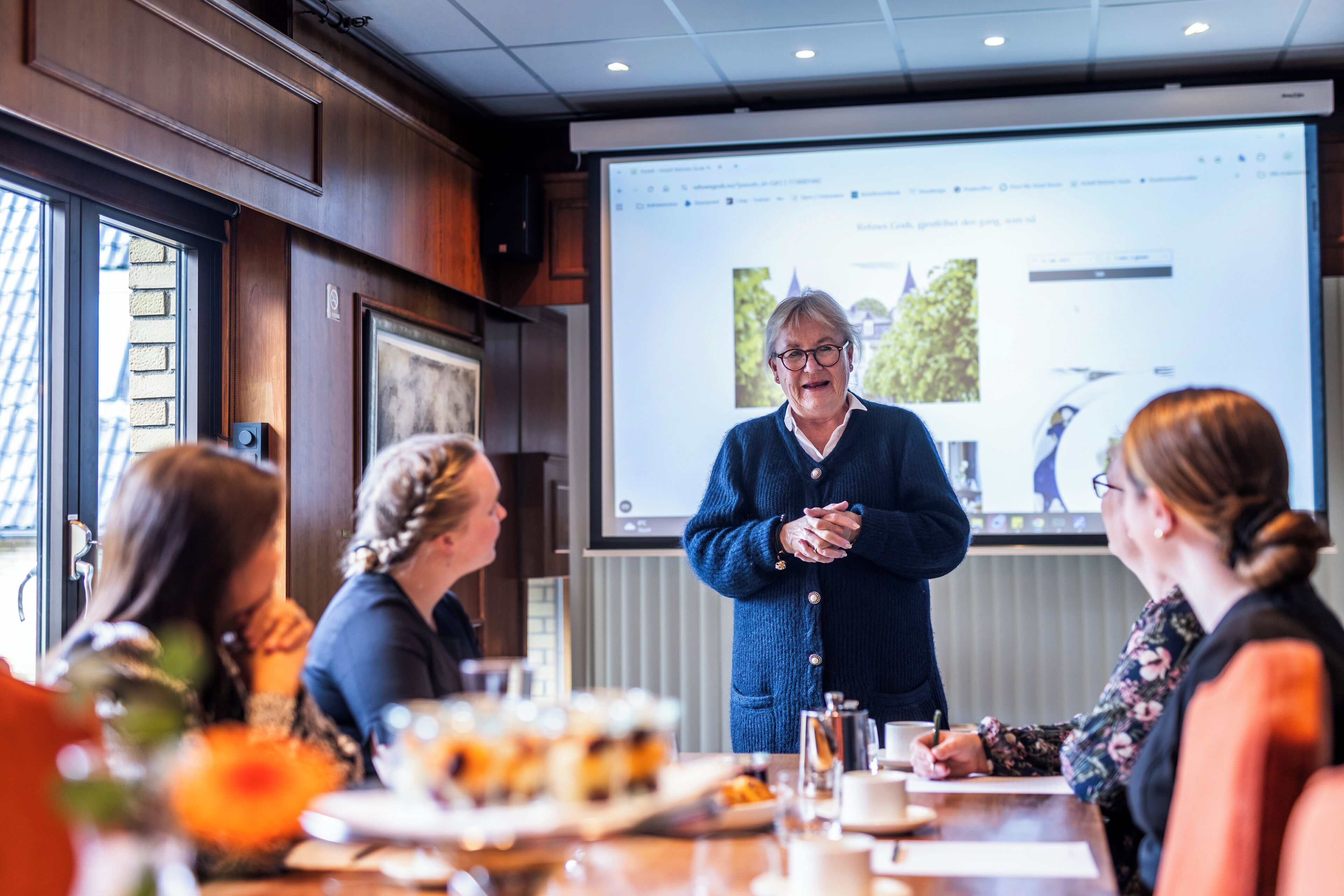 A conference room with a presentation screen, wooden paneling, and a table with food and drinks.