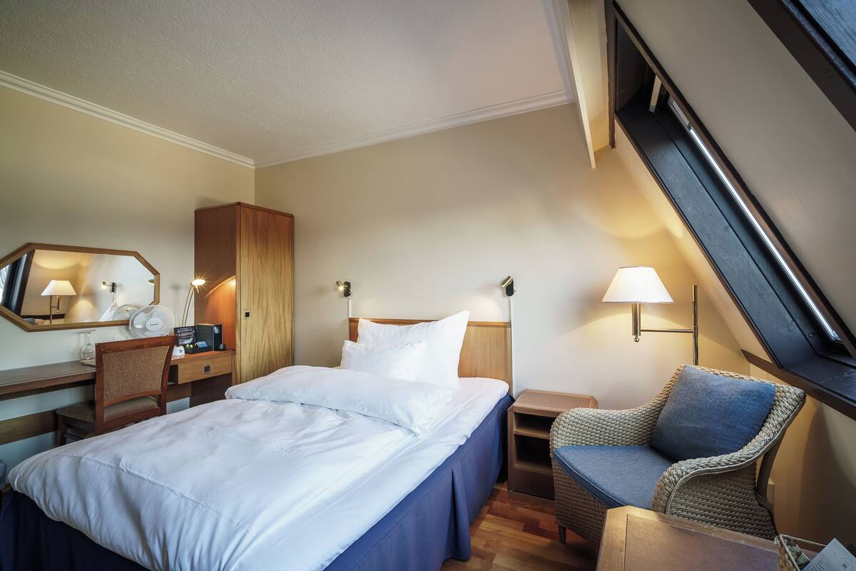 Une chambre d’hôtel comprenant un lit, un bureau, une chaise, une table de chevet et une lampe.