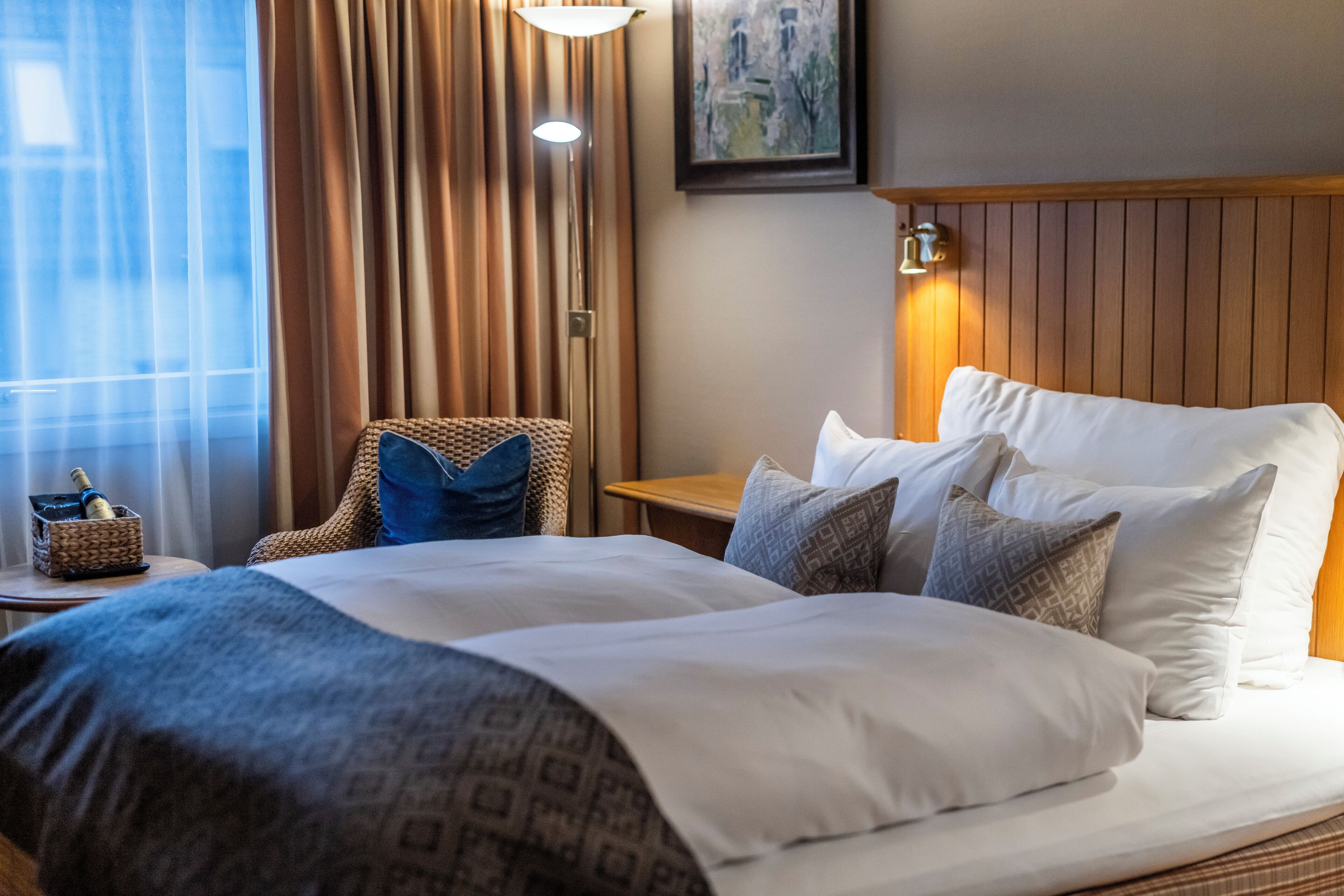 A hotel room with a large bed, a chair, a bedside table, and a lamp.