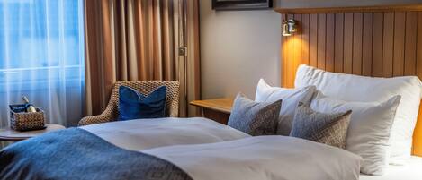 A hotel room with a large bed, a chair, a bedside table, and a lamp.