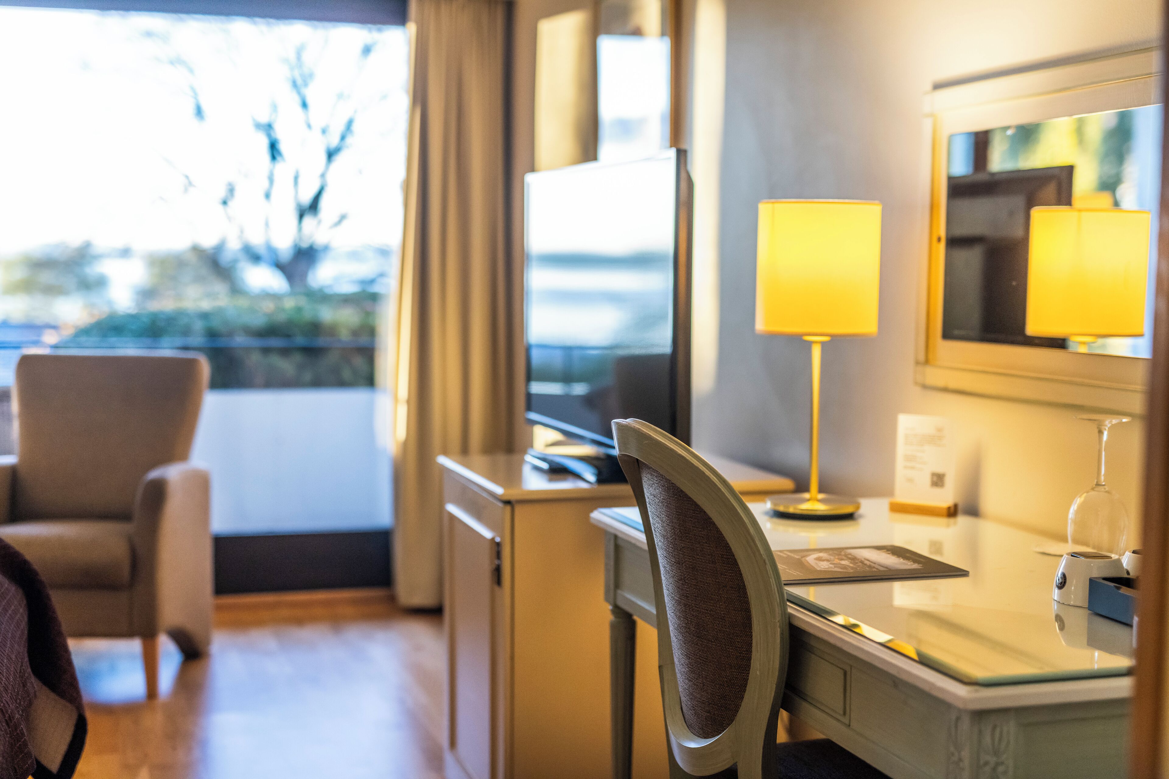 Een hotelkamer met een bureau, stoel, lamp en uitzicht op het omliggende landschap.