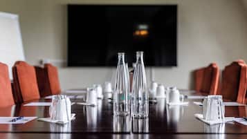 Una mesa de conferencias con botellas de vidrio transparente, servilletas blancas y una pantalla de televisión al fondo.