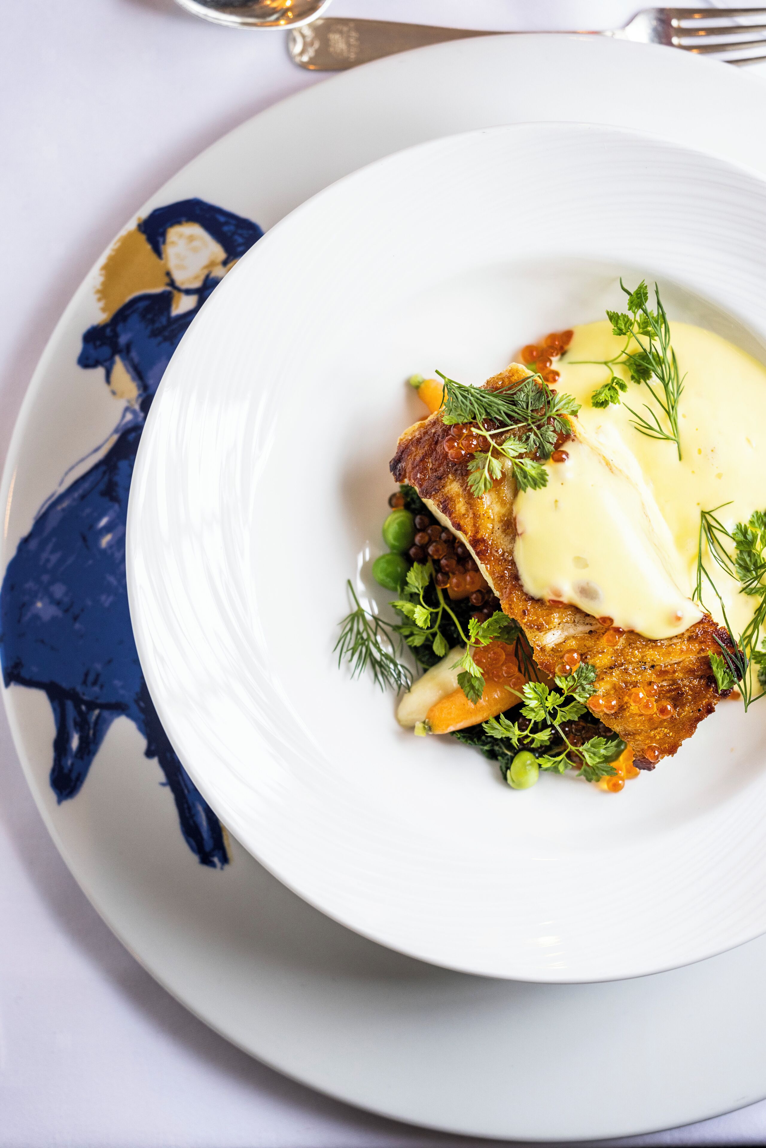 Um prato branco com carne, legumes verdes e um molho cremoso.