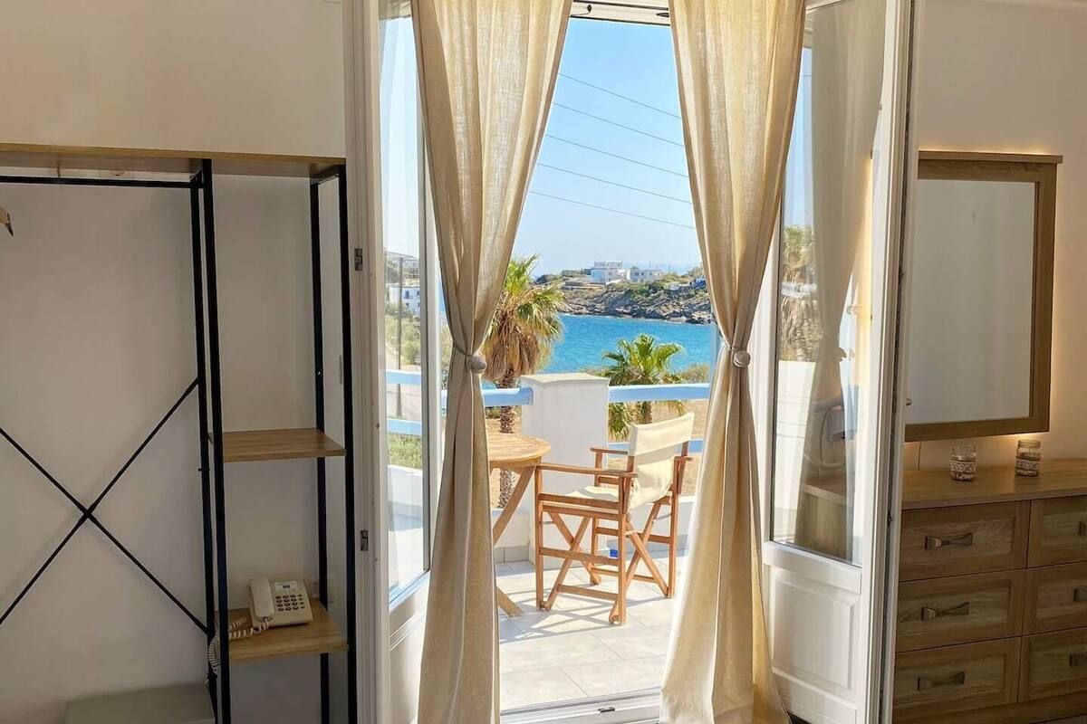A hotel room with a bed, a desk, a chair, and a view of the sea.