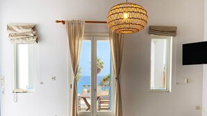 Uma sala de jantar com uma mesa posta para quatro pessoas, um lustre pendurado e vista para o mar através de uma porta de vidro.