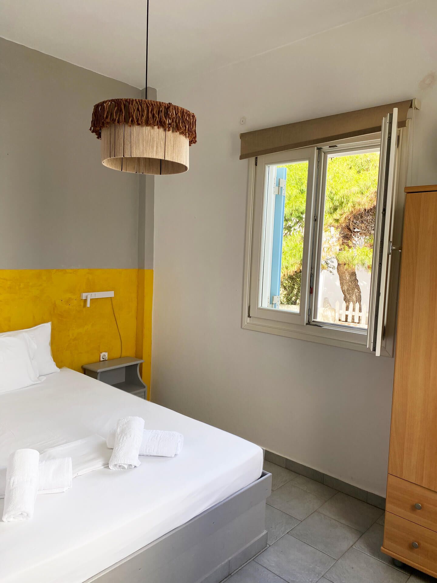 A hotel room with a bed, bedside table, lamp, window, and wardrobe.