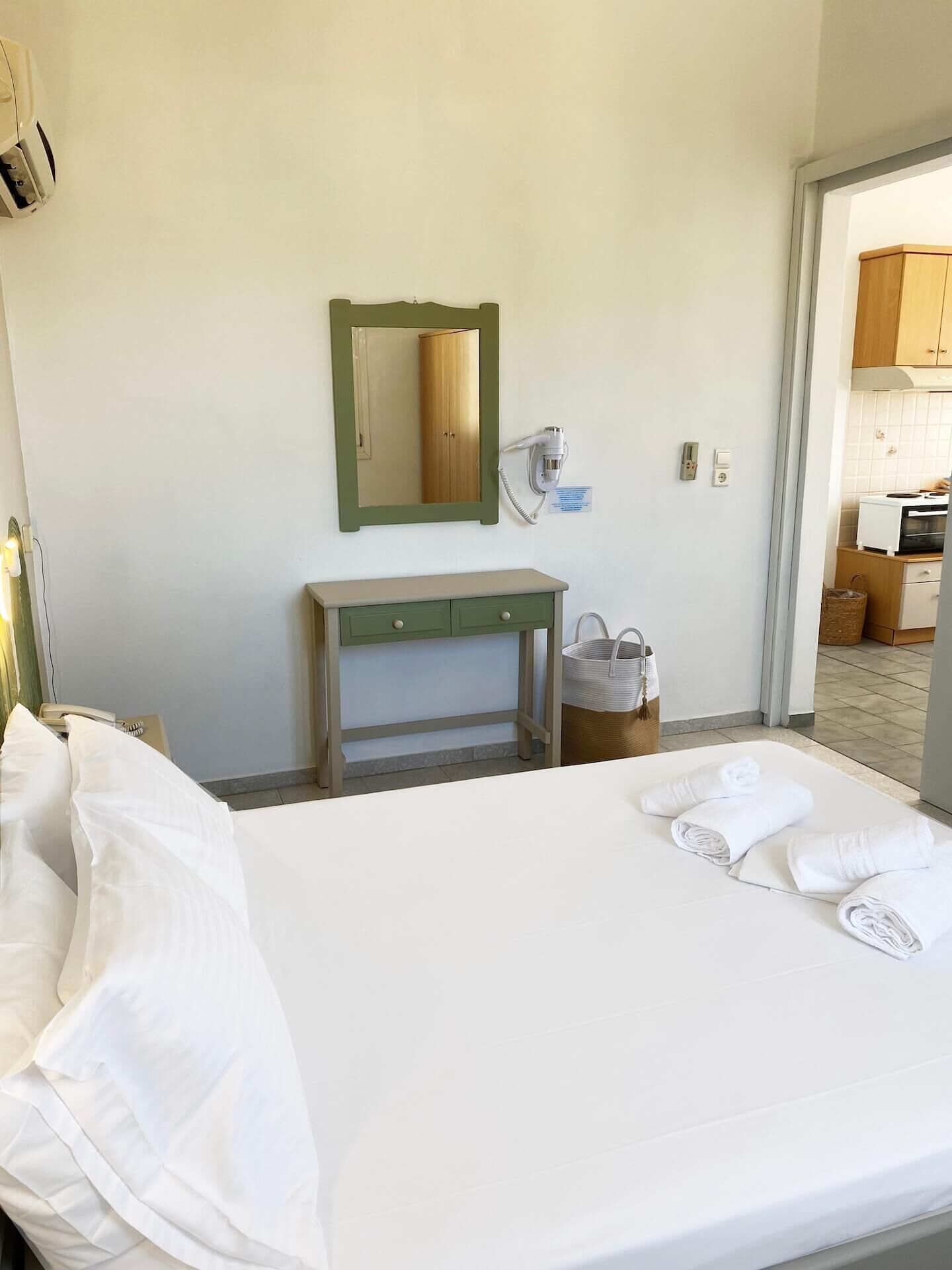 A hotel room with a bed, a bedside table, a mirror, a hairdryer, and a basket.