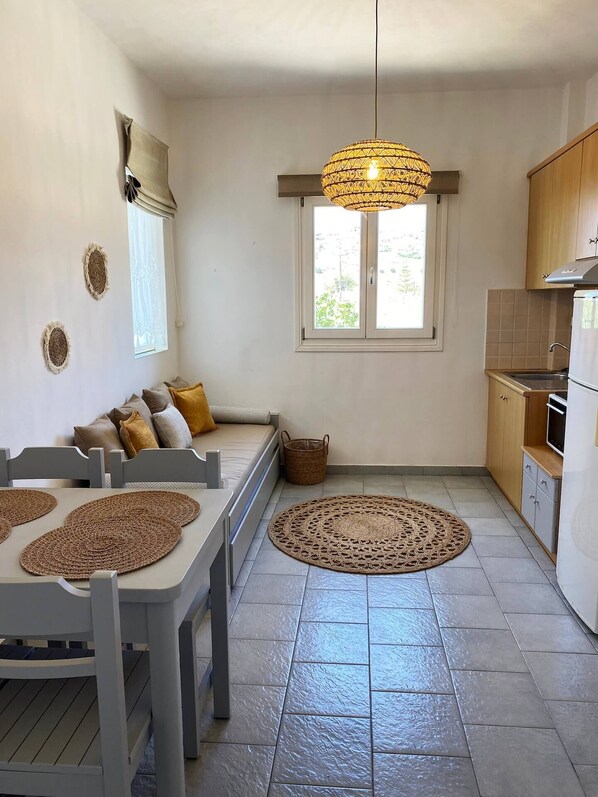 A compact kitchen with a dining area, a large window, and a hanging light fixture. - Agnadi Syros Beachfront Studios & Rooms (Syros)