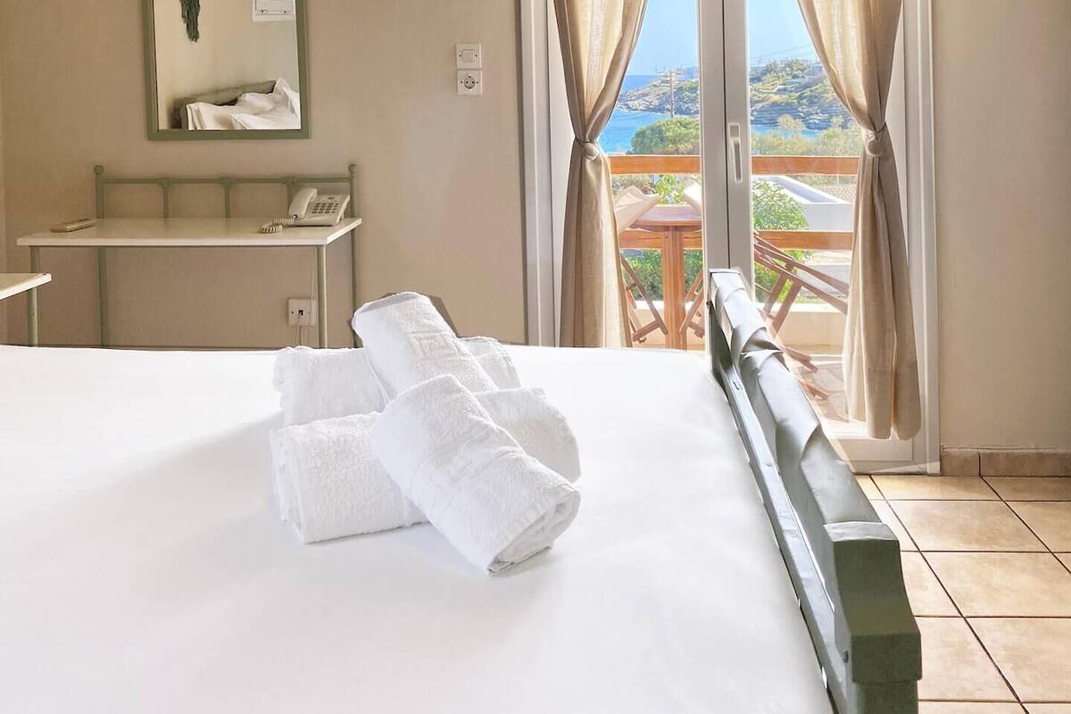 A hotel room with a bed, a desk, a mirror, and a window with curtains.