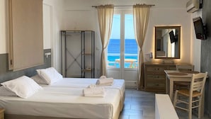 Quarto de hotel com duas camas, uma escrivaninha, uma cadeira, televisão e vista para o mar.