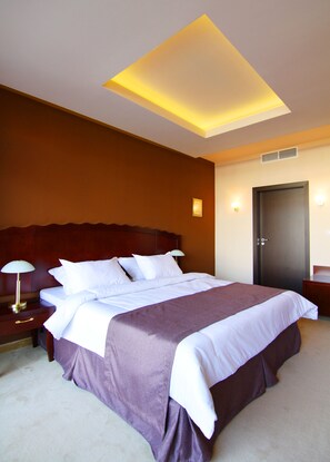 A hotel room with a large bed, a nightstand, a lamp, and a door. - The Vineyards Spa & Resort (Pomorie)