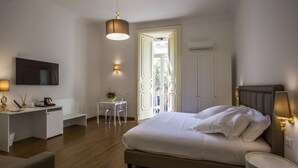 A modern hotel room with a large bed, a desk with a chair, a TV mounted on the wall, and a balcony with a view. - Napoli Class Luxury Rooms & Suites (Naples)