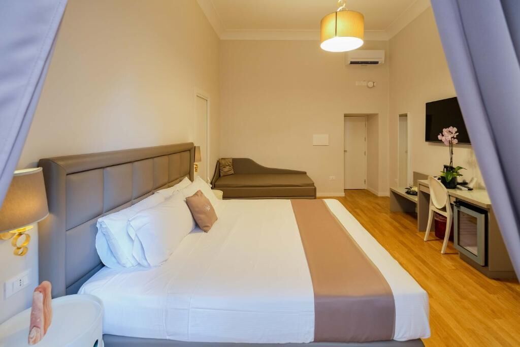 Een hotelkamer met een bed, een bureau, een stoel, een televisie en een raam met gordijnen.