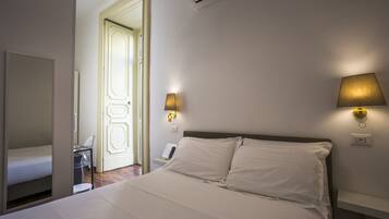A hotel room with a bed, a desk, and a chair. There is a door leading to another room and an air conditioning unit on the wall.