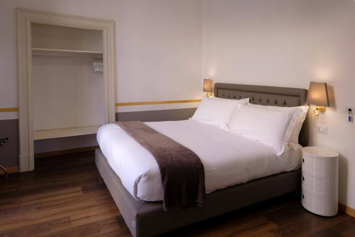 A neatly made bed with a brown throw blanket, a bedside lamp, and a white nightstand.