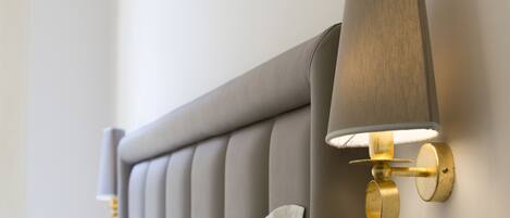 A bed with a grey upholstered headboard and a wall-mounted lamp with a cylindrical shade.