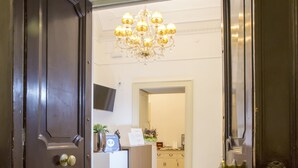 A hotel reception area with a wooden floor, a chandelier, a reception desk, and a doormat with the hotel's name. - Napoli Class Luxury Rooms & Suites (Naples)