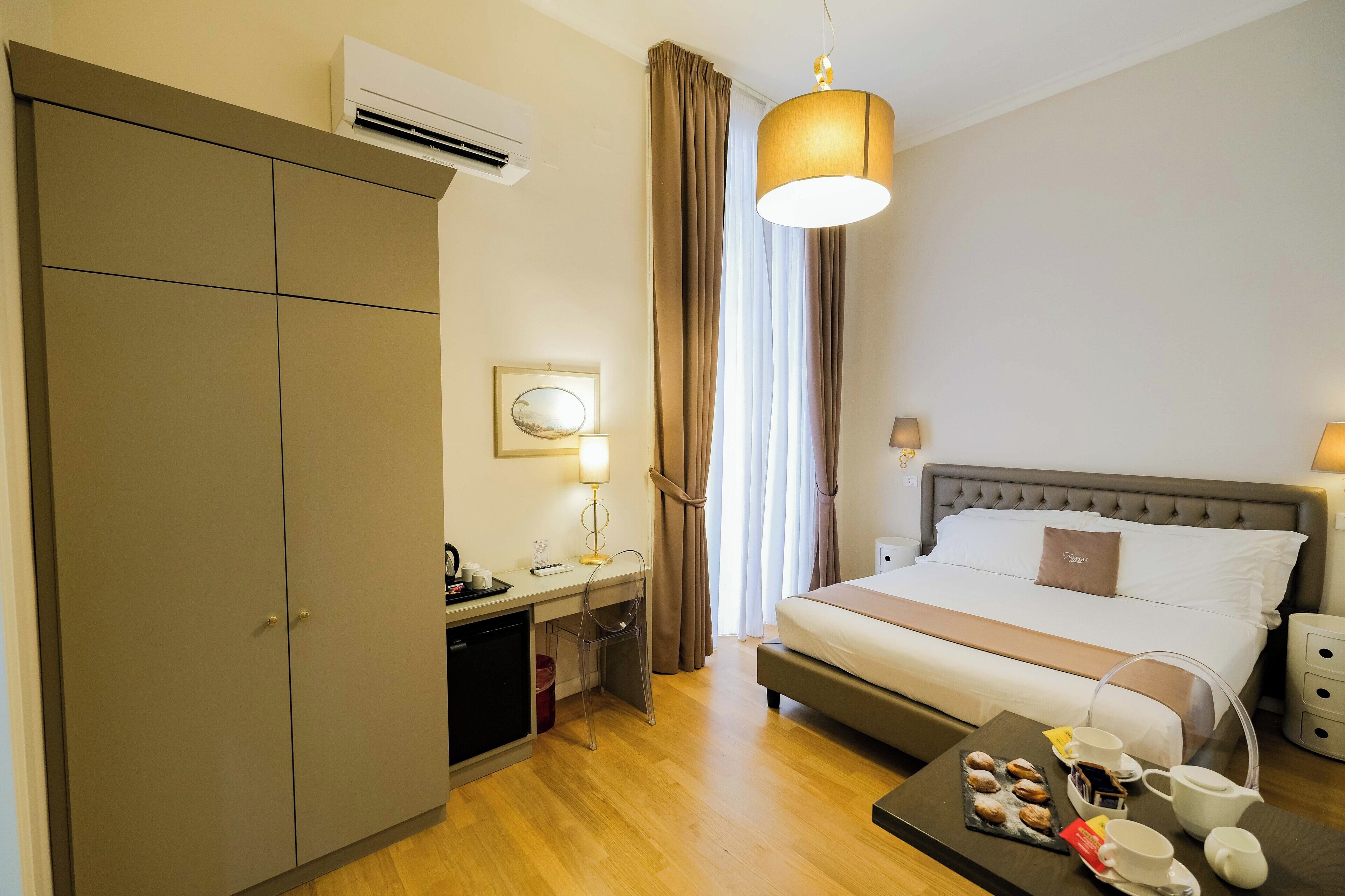 A hotel room with a bed, desk, wardrobe, and a dining table with breakfast items.
