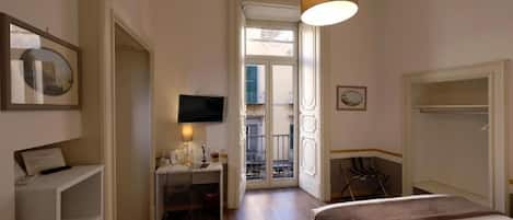 Habitación de hotel con cama, escritorio, televisor y puerta al balcón.