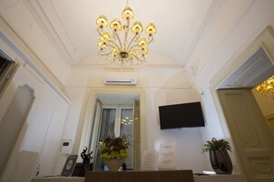 Un'area reception con un lampadario, un televisore a schermo piatto, una pianta in vaso e un cartello con testo.