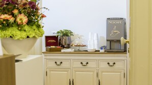 A coffee station with a Nescafé machine, cups, a cake, and a flower arrangement. - Napoli Class Luxury Rooms & Suites (Naples)
