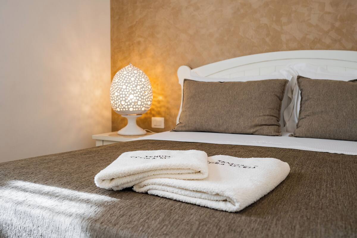 A neatly made bed with a white headboard, a textured brown bedspread, and two folded white towels on the bed.