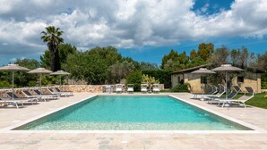 A rectangular swimming pool with clear blue water, surrounded by lounge chairs and umbrellas, set against a backdrop of trees and a stone wall. - Tenuta Flora Maria (Leverano)