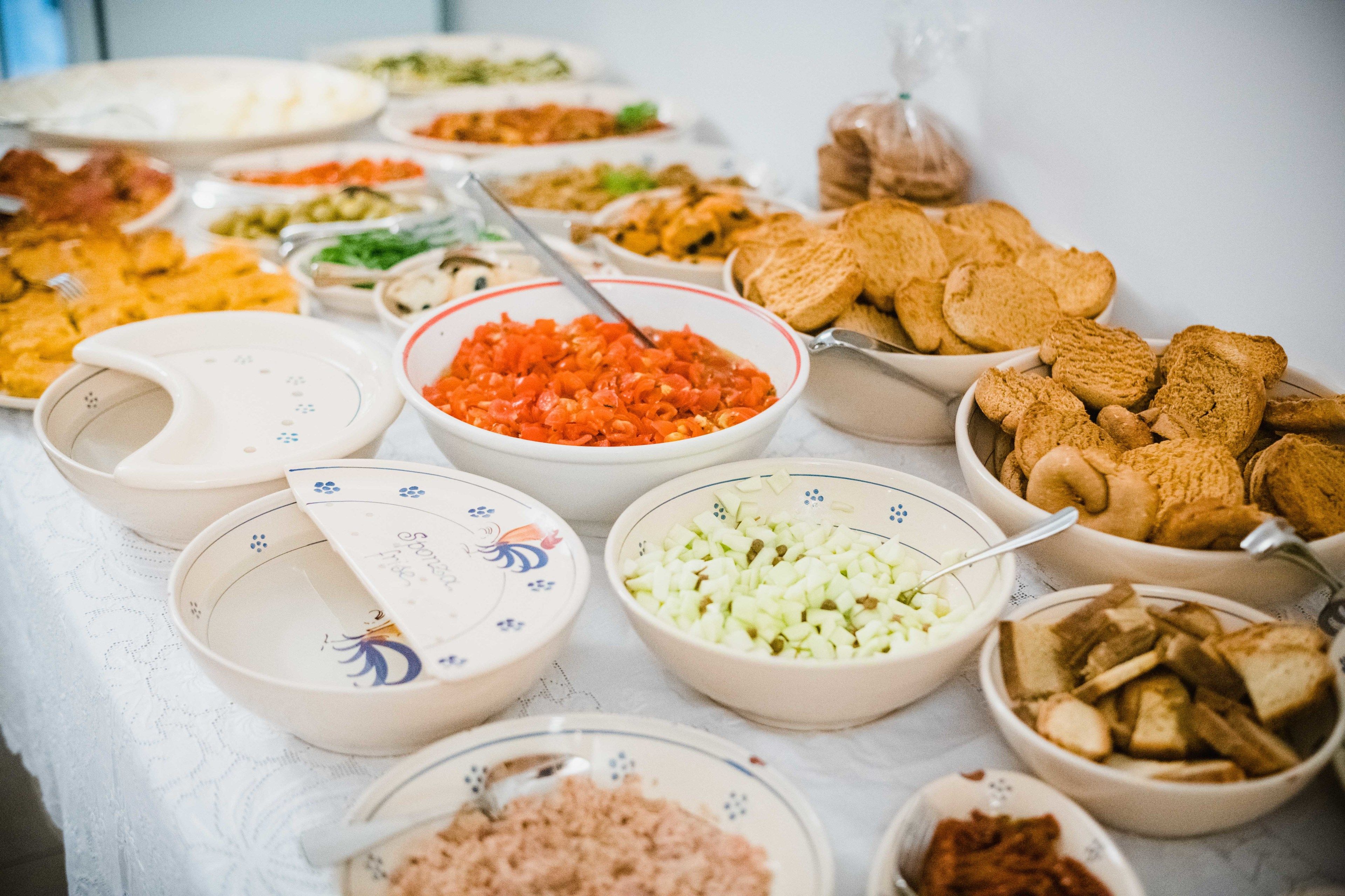 A table with various dishes and bowls of food, including sliced vegetables and bread.