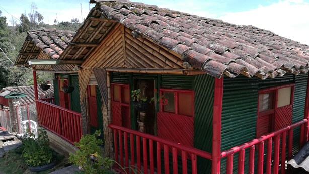 Una casa rustica in legno con tetto in tegole, un balcone rosso e una porta verde.