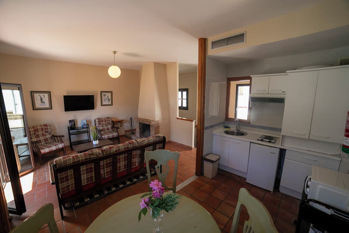 Una sala de estar con un sofá, una mesa de comedor con flores y una cocina con armarios blancos y un refrigerador pequeño.