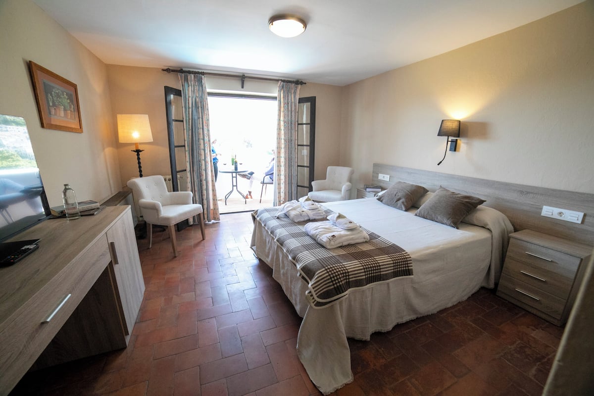 Habitación de hotel con cama, mesitas de noche, escritorio, silla, lámpara y vistas al exterior.