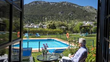 A pool area with a view of mountains, outdoor seating, and a table with flowers.