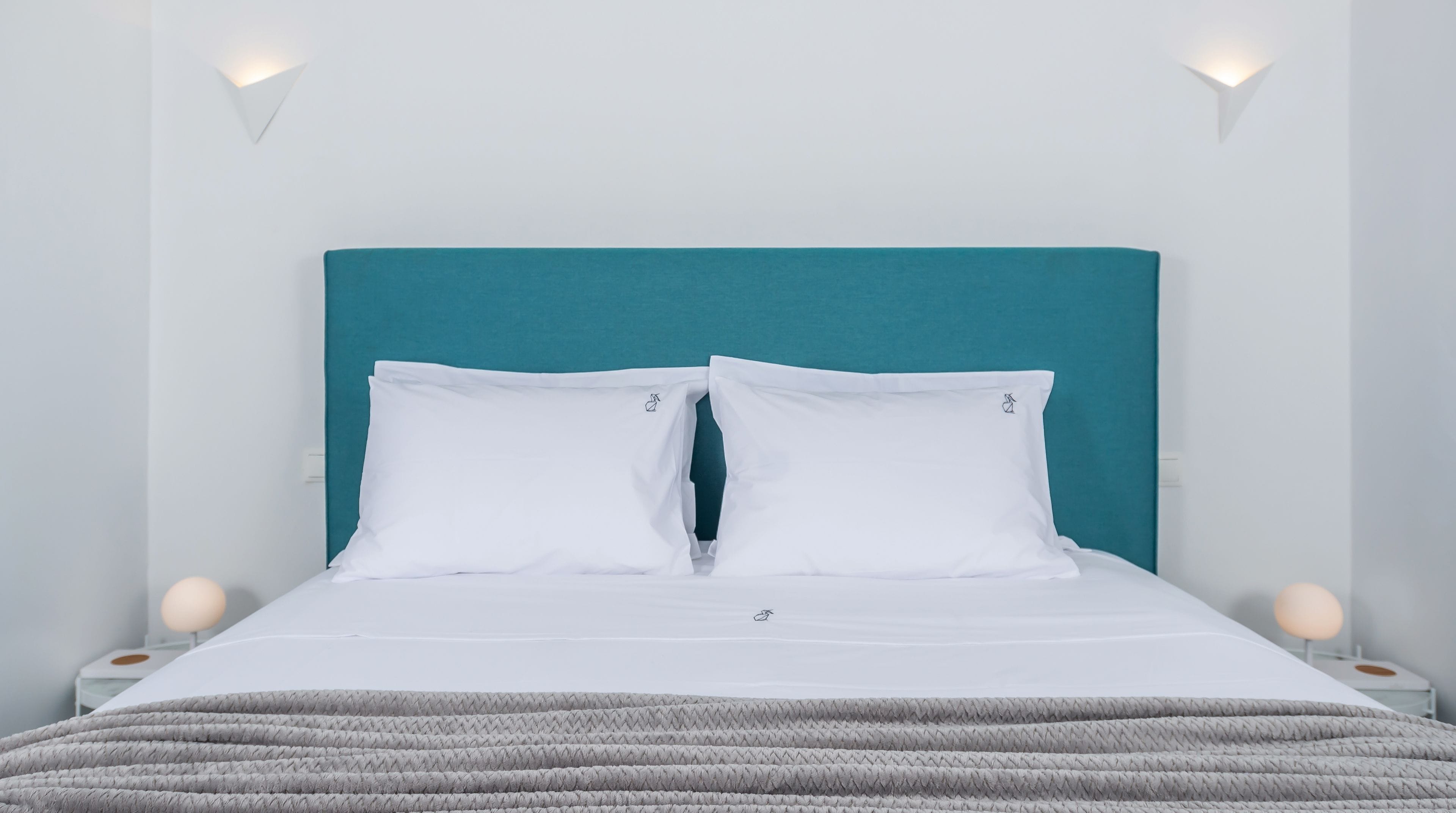 A neatly made bed with white bedding and a teal headboard.