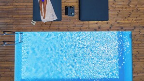 Un área junto a la piscina con un deck de madera, una silla de descanso, una toalla y un traje de baño.