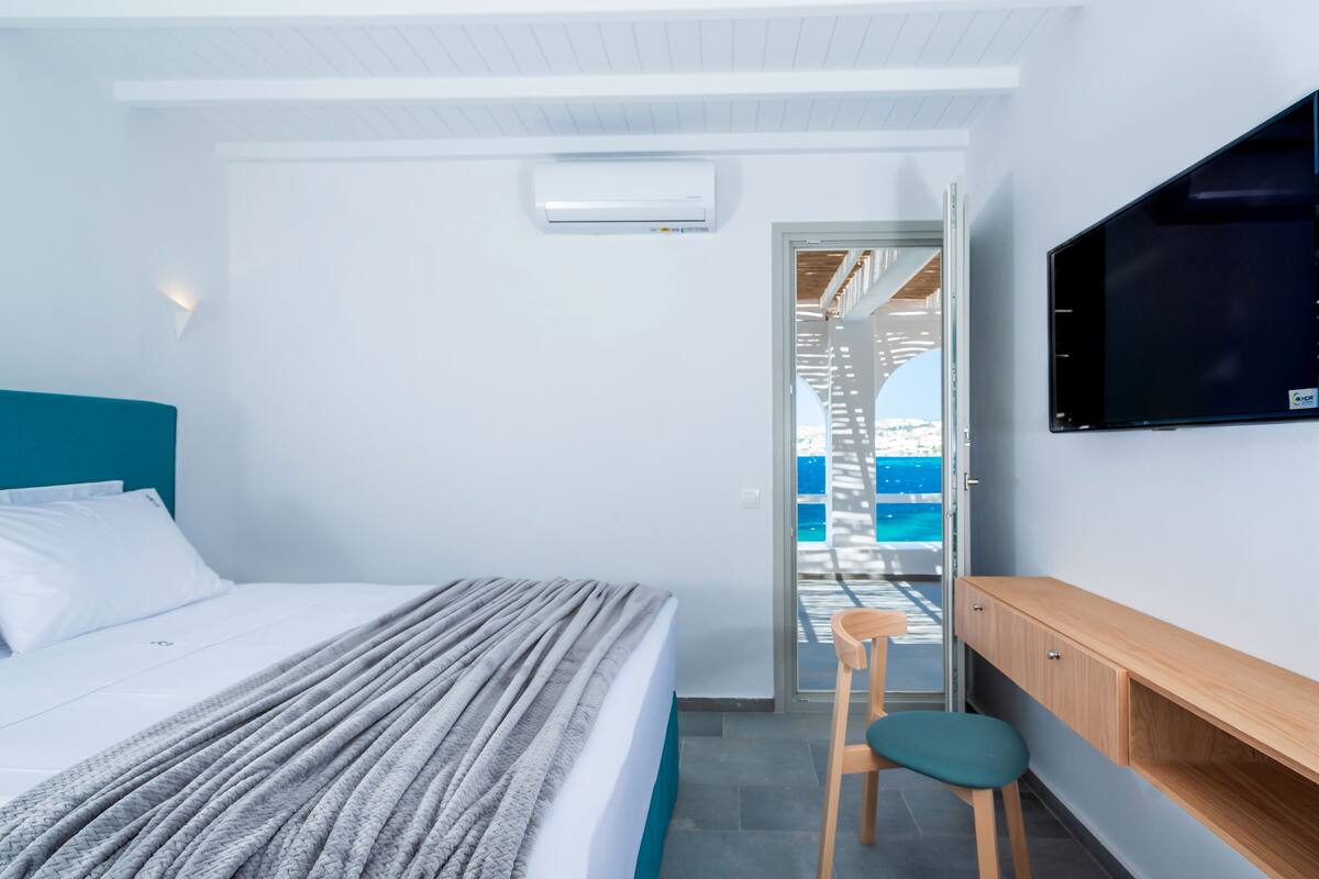A bedroom with a bed, a TV mounted on the wall, a desk, and a chair.