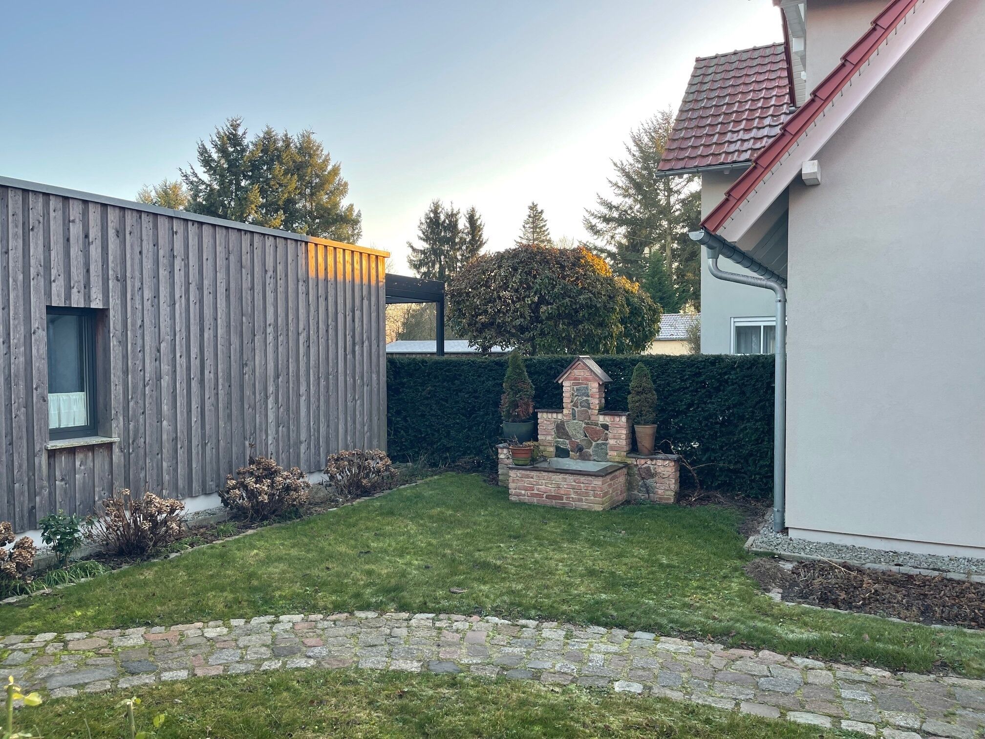 Una casa moderna con fachada de madera, un elemento decorativo de piedra en el jardín y un césped bien cuidado.