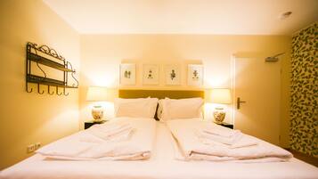 A hotel room with a bed, two bedside tables with lamps, a wall-mounted shelf, and framed botanical prints above the bed.