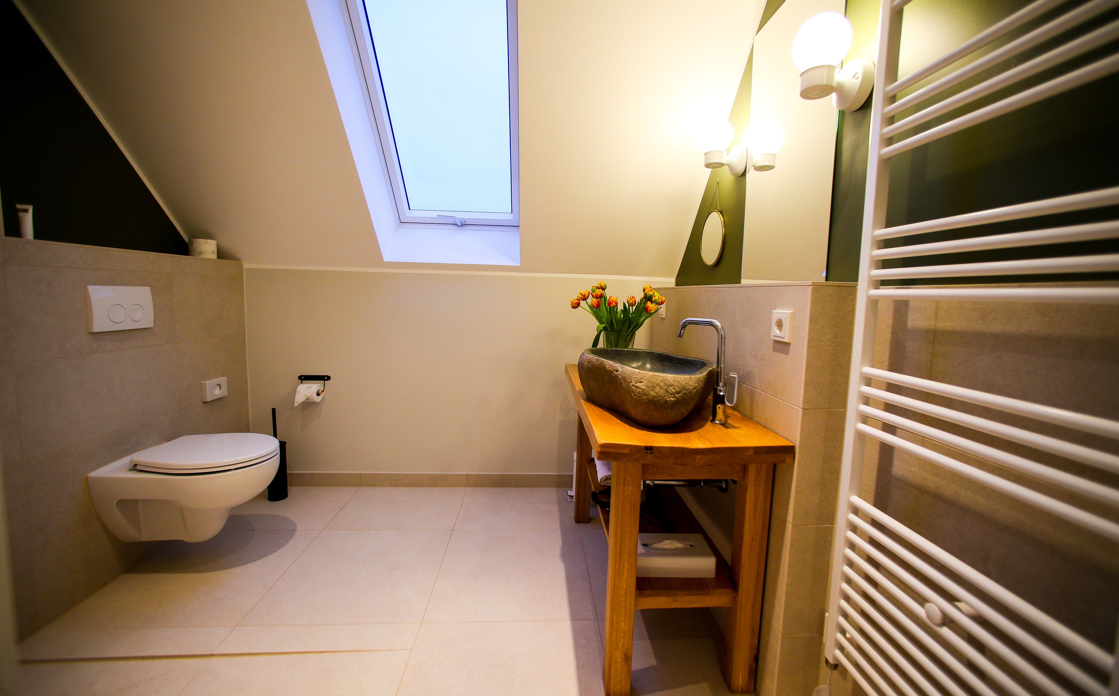 A compact bathroom with a toilet, a wooden vanity with a stone basin, a small window, and a towel rack.