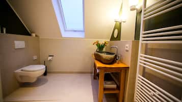 A compact bathroom with a toilet, a wooden vanity with a stone basin, a small window, and a towel rack.
