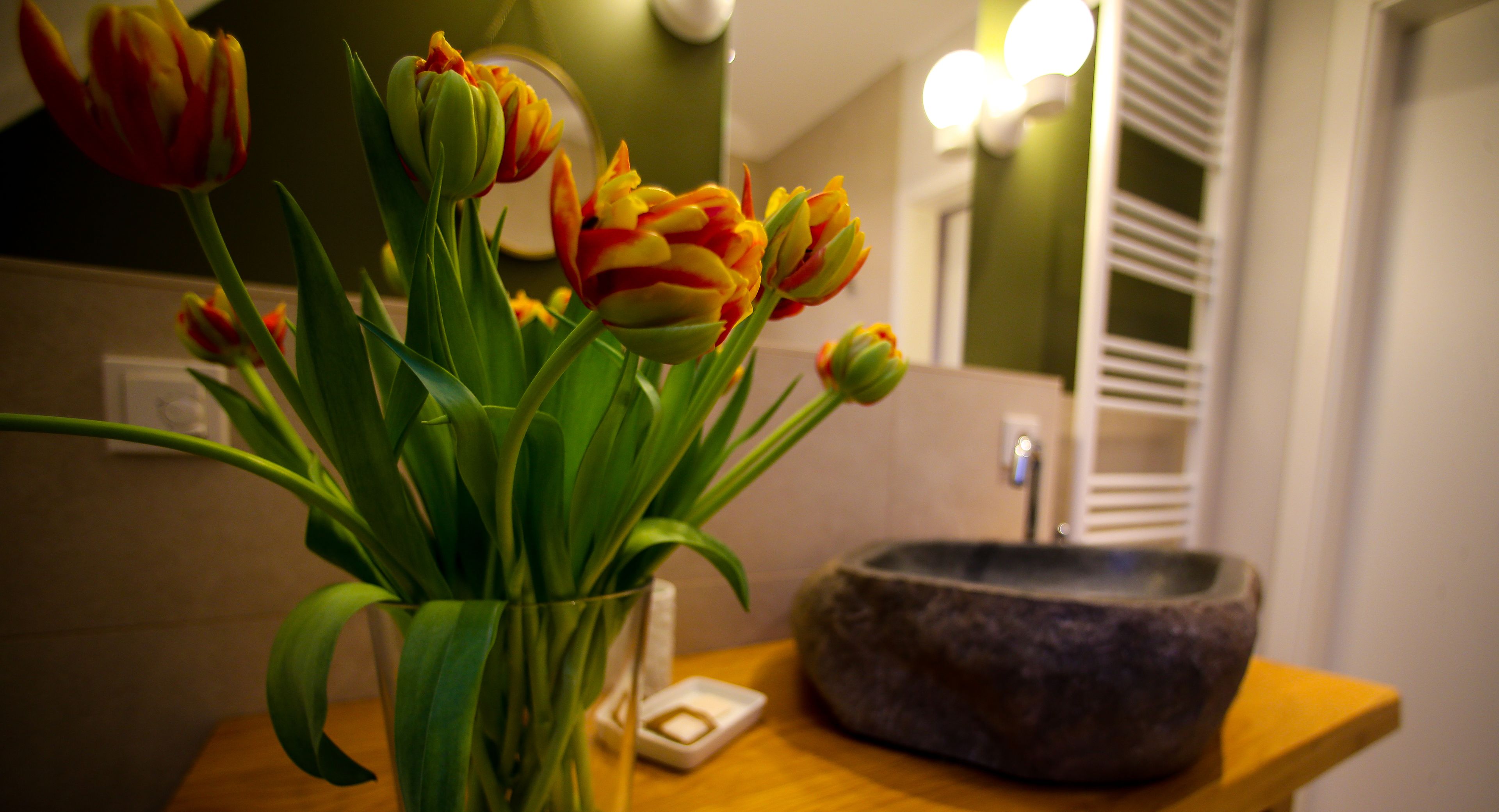 A bathroom with a glass vase of tulips, a soap dish, and a stone sink.