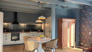 A modern kitchen with white cabinets, a black range hood, and a round dining table with wicker chairs.