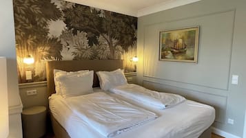 A neatly made bed in a hotel room with a floral wallpaper, two bedside lamps, and a painting on the wall.