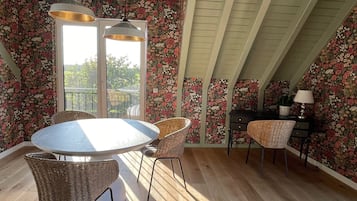 Un comedor con una mesa redonda, sillas de mimbre y vistas al balcón exterior a través de un ventanal.