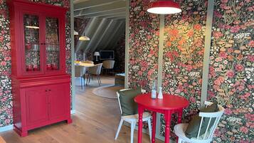 Een eetgedeelte met een rode tafel en stoelen, een rode kast en bloemenbehang.