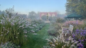Un sendero en un jardín que lleva a una casa roja con valla blanca y un paraguas verde.
