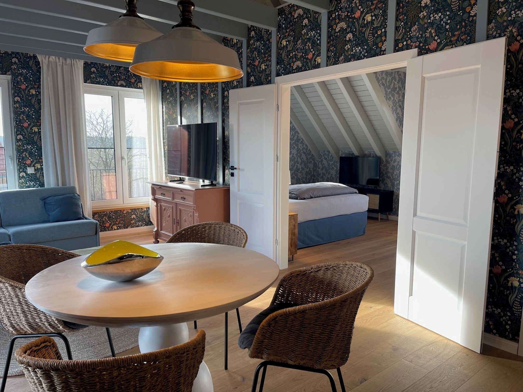 A cozy room with a dining table, wicker chairs, a sofa, and a bed.