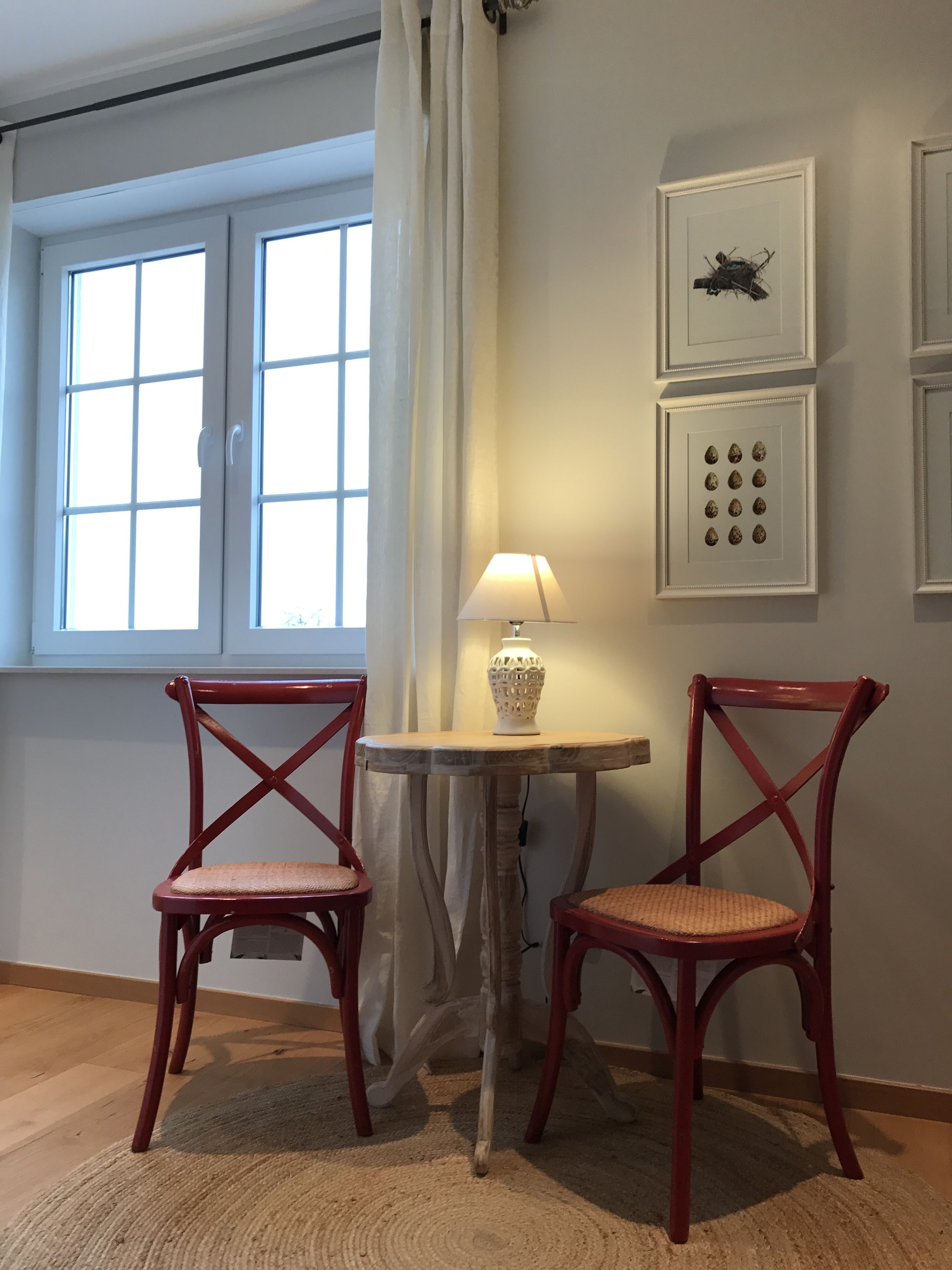 A room with two wooden chairs, a small table with a lamp, and a window with curtains.