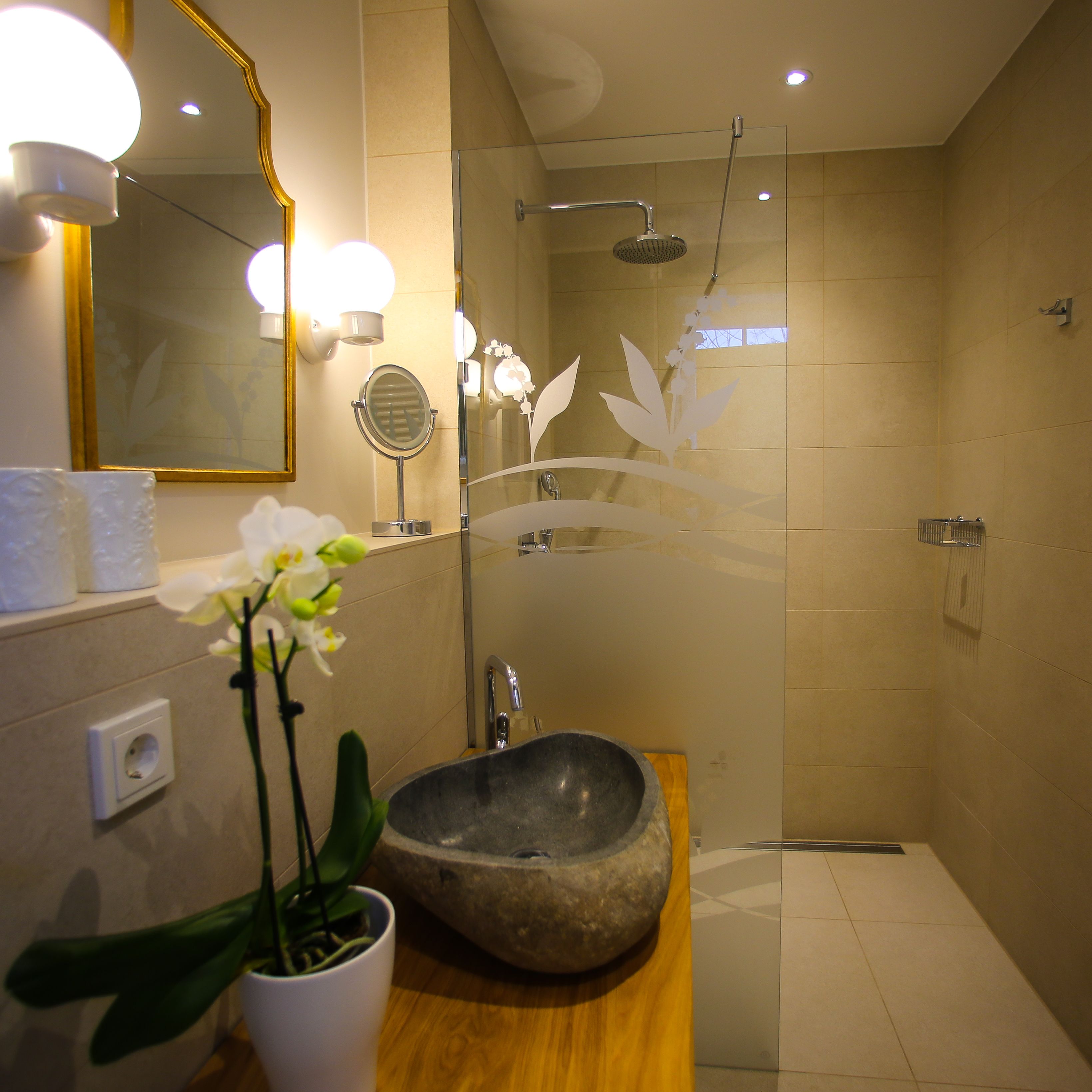 A modern bathroom with a stone sink, a handheld mirror, a wall-mounted light, and a shower area.